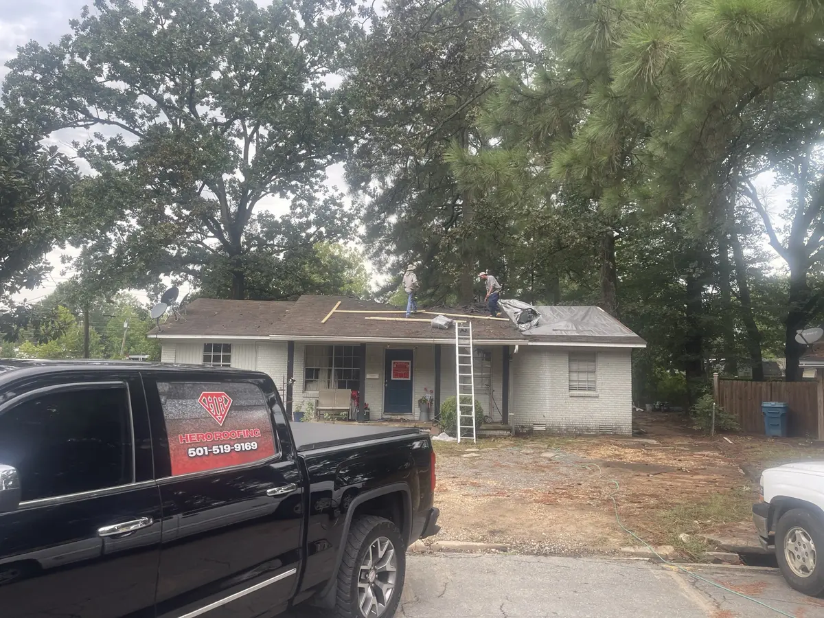 Hero Roofing crew replacing the roof on a brick home in Central Arkansas, with the company truck parked in front